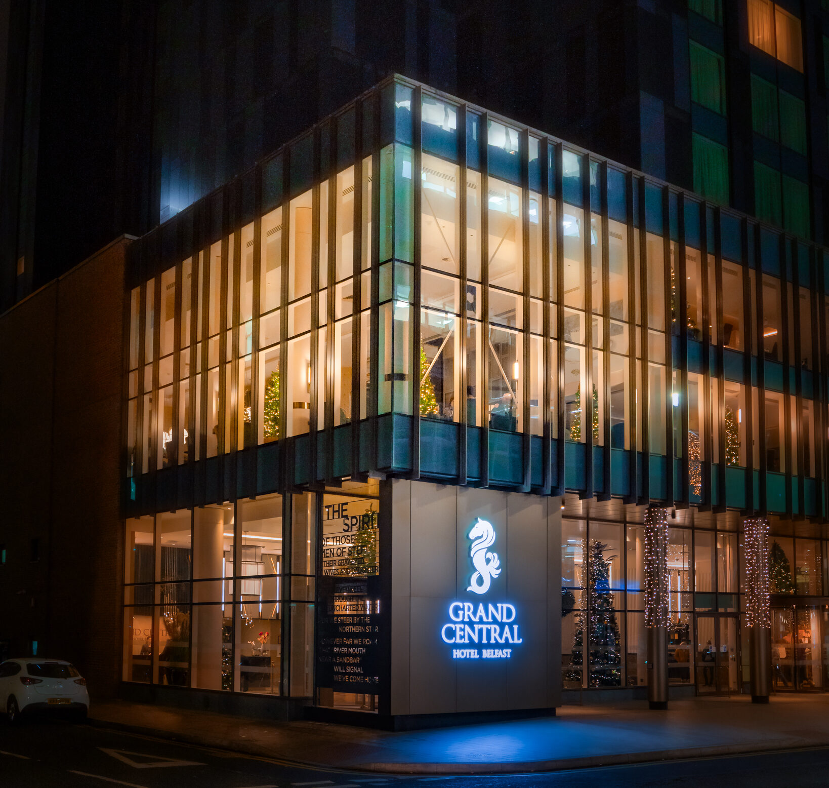 Night view of the Grand Central Hotel Belfast exterior with visible lights and glass facade.